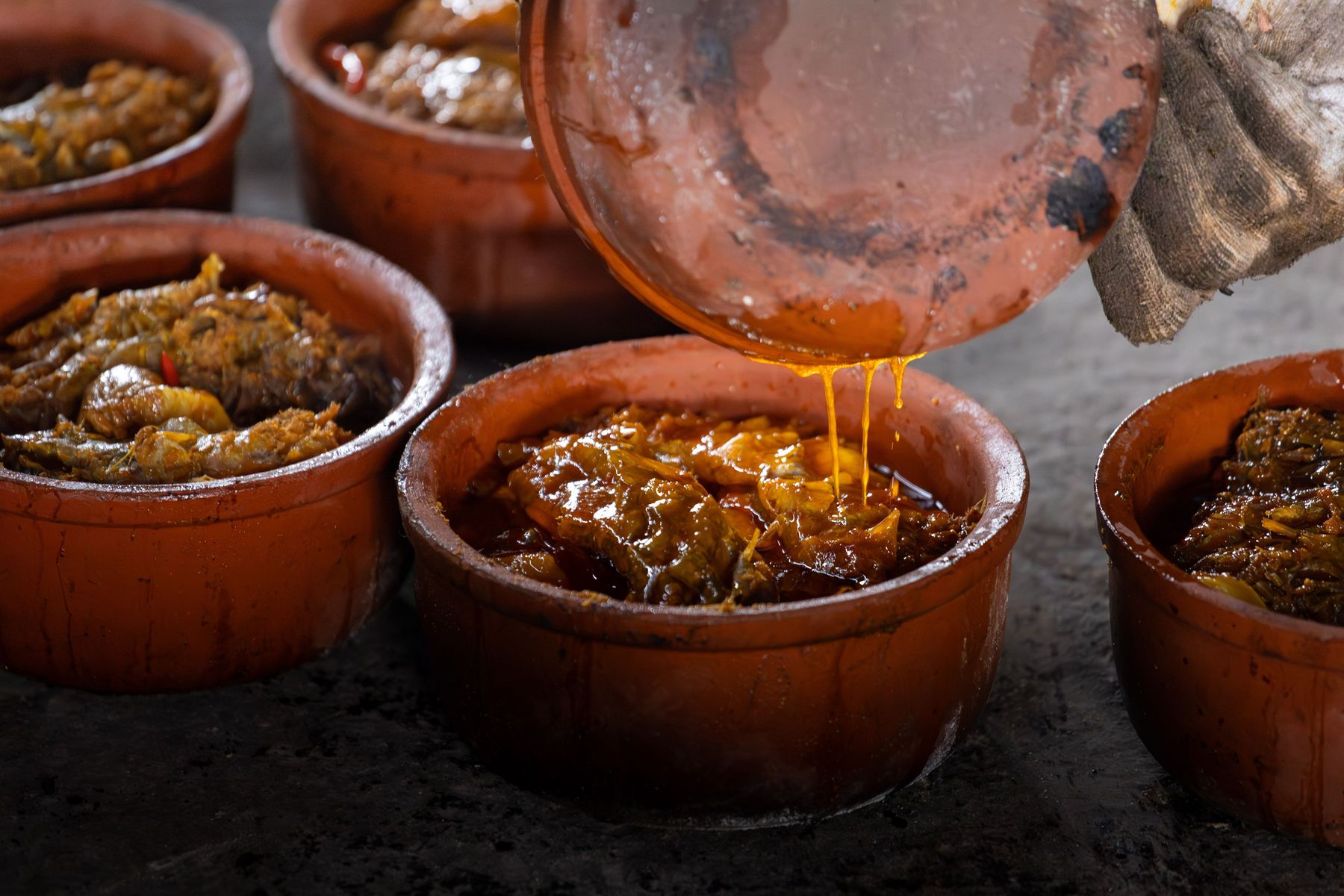 Sauce being poured over glazed meat in a clay cooking pot, illustrative photography