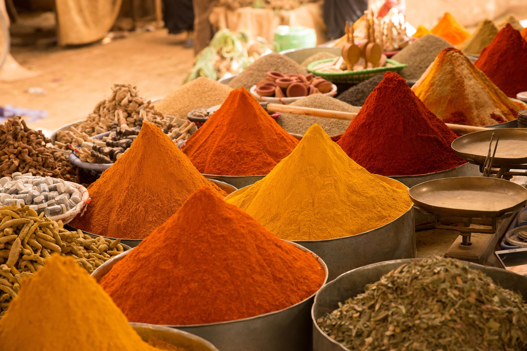 Colourful mounds of ground spices — chilli, turmeric, paprika — at an outdoor market stall, illustrative photography